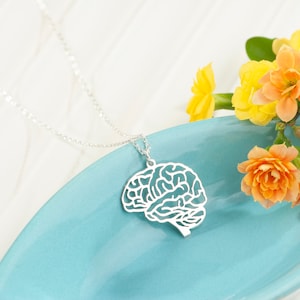 Peut inclure: Un collier en argent avec un pendentif en forme de cerveau sur une assiette bleue avec des fleurs orange.