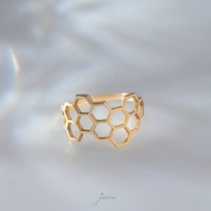 May include: A gold-toned ring with a honeycomb design. The ring is made of metal and has a geometric pattern.
