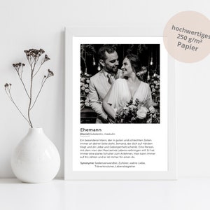 May include: A framed black and white photograph of a couple embracing, with text below describing the term "husband." The print is displayed on a white surface, with a white vase holding dried flowers to the left.
