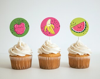 May include: Three cupcakes decorated with fruit-themed toppers. The cupcakes are white with vanilla frosting. The toppers are round and feature a raspberry, a banana, and a watermelon.