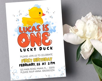 Puede incluir: Una tarjeta de invitación blanca con un pato de goma amarillo en una bañera azul con burbujas. El texto de la tarjeta dice "Lucas tiene un año, un pato con suerte" e incluye detalles para una fiesta de primer cumpleaños.