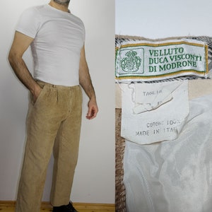Op de afbeelding: Beige corduroy broek met een geplooide voorkant en een label met de tekst "Velluto Duca Visconti Di Modrone", "Taglia 32", "Cotone 100%" en "Made in Italia".