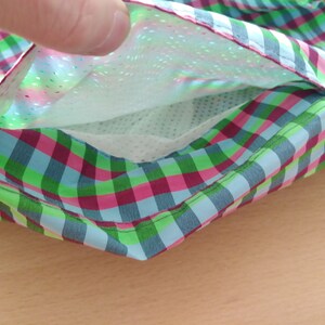 May include: A close-up of a green, pink, and blue plaid fabric with a white mesh pocket lining. The pocket is open and the fabric is folded over.
