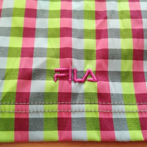May include: A close-up of a pink, green, and gray checkered fabric with the word "FILA" embroidered in pink.