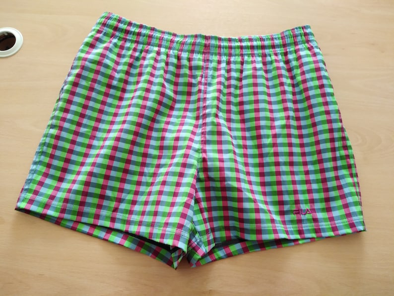 May include: Green, pink, and blue checkered swim trunks with a white "FILA" logo on the right side.