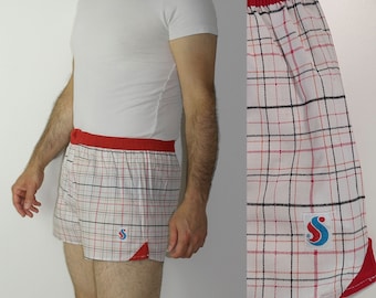 Può includere: Boxer in tessuto bianco e rosso a quadri con una cintura rossa e un logo blu e rosso che dice "S".