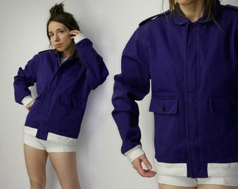 May include: A purple utility jacket with a white lining and two large pockets. The jacket has a zipper closure and a button-up collar.