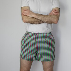 May include: A pair of checkered swim trunks with a green, blue, and pink pattern. The trunks have a drawstring waist and a relaxed fit.