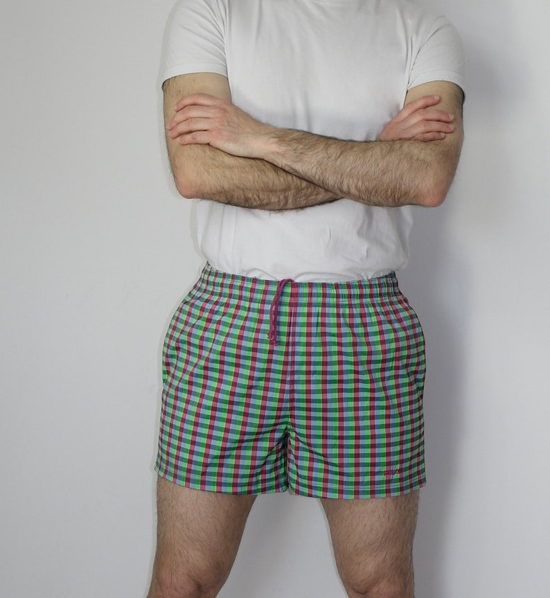 May include: A pair of checkered swim trunks with a green, blue, and pink pattern. The trunks have a drawstring waist and a relaxed fit.