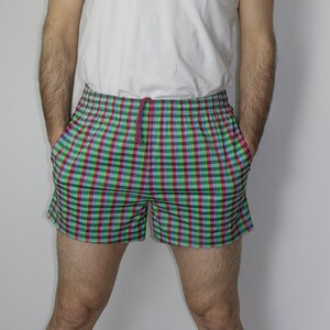 May include: A pair of plaid swim trunks with a green, blue, and red checkered pattern. The trunks have a drawstring waistband and are made of a lightweight fabric.