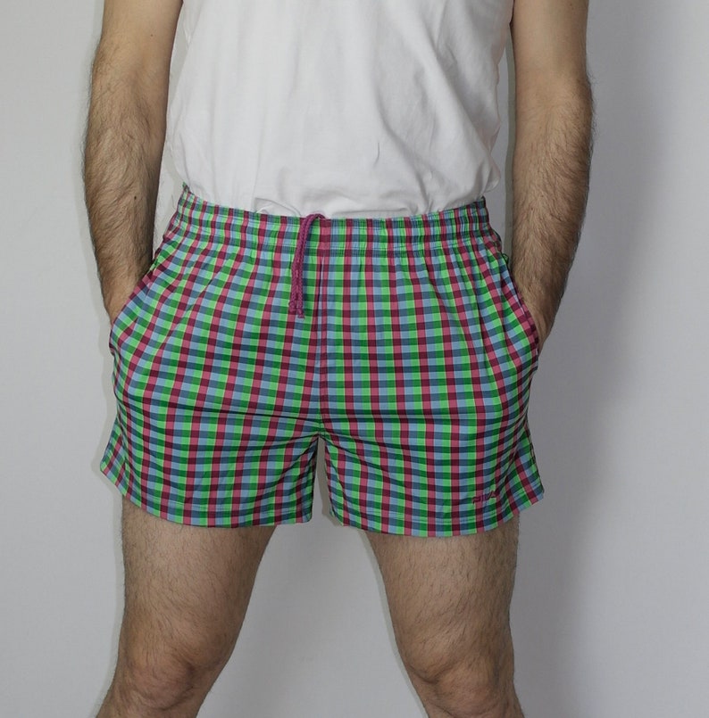 May include: A pair of plaid swim trunks with a green, blue, and red checkered pattern. The trunks have a drawstring waistband and are made of a lightweight fabric.