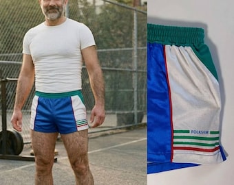 May include: Blue, white, and green athletic shorts with red and white stripes. The shorts have a white panel on the side with the word "FOLKSAM" printed in green. The shorts are paired with white socks with red and blue stripes.