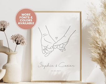 May include: A framed art print featuring a minimalist line drawing of two hands holding pinky fingers, with a small heart above. The names "Sophie & Conor" and the date "12.12.2023" are below. The text "MORE FONTS & COLORS AVAILABLE" is in a circular shape.