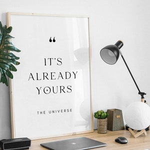 Könnte beinhalten: Ein gerahmter Druck mit weißem Hintergrund und schwarzem Text, der "It's already yours - The Universe" lautet. Der Druck befindet sich auf einem Schreibtisch mit einer Lampe, einer Topfpflanze und einer Mondlampe.