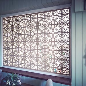 May include: A decorative window screen with a repeating, ornate pattern. The screen is made of a dark material and is set within a white frame. The intricate design allows light to filter through, creating a visually appealing effect.