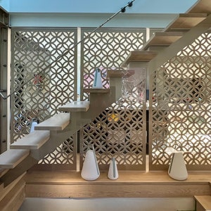 May include: A modern staircase with light wood steps and a metal frame. The design includes decorative panels with a circular pattern. White, teardrop-shaped lamps are placed on the landing and the floor below the stairs.