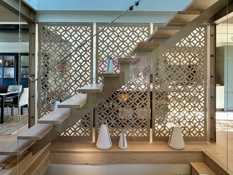 May include: A modern staircase with light wood steps and a metal frame. The design includes decorative panels with a circular pattern. White, teardrop-shaped lamps are placed on the landing and the floor below the stairs.