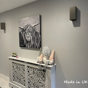 May include: A monochrome painting of a Highland cow on a grey wall, with two grey wall lights. Below, a decorative radiator cover and gnomes are visible. The text "Made in UK" is in the bottom right corner of the image.