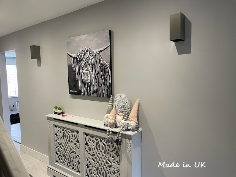 May include: A monochrome painting of a Highland cow on a grey wall, with two grey wall lights. Below, a decorative radiator cover and gnomes are visible. The text "Made in UK" is in the bottom right corner of the image.