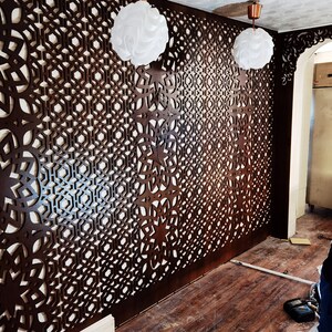 May include: A room with dark brown, intricately patterned wooden wall panels. Two white, spherical pendant lights hang from the ceiling. The floor is made of wooden planks. The design is geometric and creates a decorative screen.