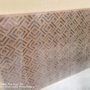 May include: A rectangular wooden panel with a geometric pattern of repeating diamond shapes. The panel is a warm brown color and appears to be wrapped in clear plastic. The design is cut out of the wood, creating a textured surface.