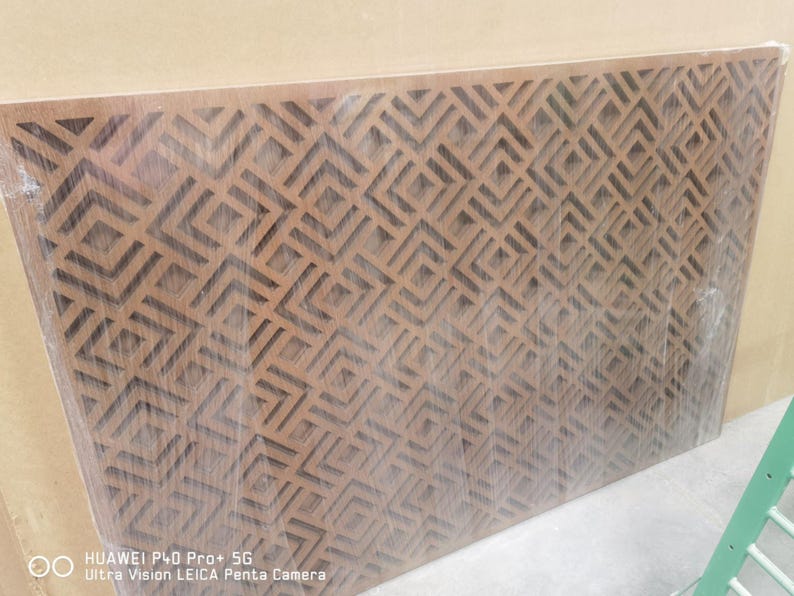 May include: A rectangular wooden panel with a geometric pattern of repeating diamond shapes. The panel is a warm brown color and appears to be wrapped in clear plastic. The design is cut out of the wood, creating a textured surface.