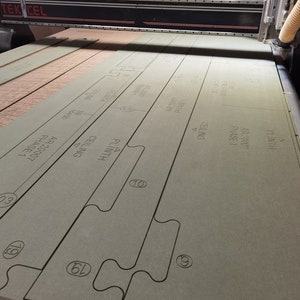 Peut inclure: Gros plan sur une planche à découper verte avec différentes formes découpées. La planche est étiquetée avec le texte "AR 20007 Phase 1", "Plafond", "Plinthe" et "Fluith".