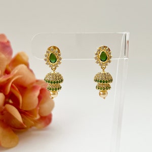 May include: A pair of gold earrings with green and white stones. The earrings are in the shape of a teardrop with a small pearl at the bottom.