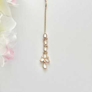 May include: A gold chain with a teardrop-shaped pendant adorned with clear, faceted stones. The pendant is surrounded by smaller, clear stones.