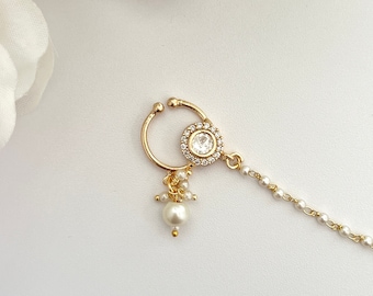 May include: Gold nose ring with a clear rhinestone and a pearl drop. The ring is attached to a delicate chain of small white pearls.