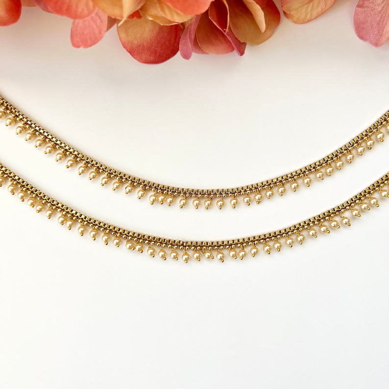 Pu&ograve; includere: Un paio di cavigliere dorate con delicati accenti di perle. Le cavigliere presentano un design a catena con piccole perle pendenti.