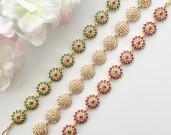 May include: Three gold hair chains with decorative floral designs. Each chain features a different colored gemstone: green, white, and pink.