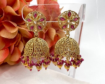 May include: Gold earrings with a pink flower design and dangling pink beads. The earrings are on a white background.