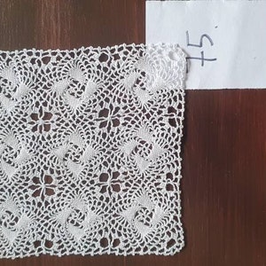 Könnte beinhalten: Ein weißes quadratisches Häkeldeckchen mit einem zarten Blumenmuster. Das Deckchen liegt auf einer braunen Holzoberfläche. Das Preisschild zeigt "5 €".