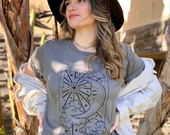 May include: A gray t-shirt with a black and white illustration of the tarot card "The Moon". The card features a crescent moon with a face, a star, and clouds.
