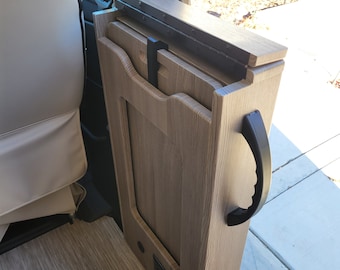 Könnte beinhalten: Ein klappbarer Holztisch mit einem schwarzen Griff, der in einem Wohnmobil verstaut ist. Der Tisch ist aus hellem Holz mit einer Holzmaserung. Der Tisch ist zusammengeklappt und steht senkrecht.