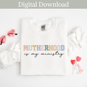 May include: White sweatshirt with the text "MOTHERHOOD is my ministry" in colorful letters. The letters are outlined in black and have a vintage look.