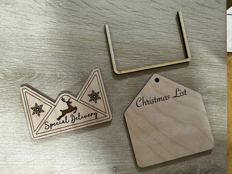 May include: A wooden Christmas list tag with the text "Christmas List" and a wooden envelope with the text "Special Delivery" and a reindeer and snowflake design.