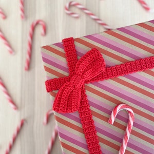 May include: A red and white striped gift box with a red crocheted bow and a red and white candy cane on top.