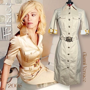 Könnte beinhalten: Ein beigefarbenes Hemdbkleid mit Gürtel und goldenen Akzenten. Das Kleid hat einen Kragen und kurze Ärmel mit einem gelben und weißen Muster. Der Text "Gianni Versace" ist auf der rechten Seite des Bildes gedruckt. Der Text "2005" ist unten links im Bild gedruckt.