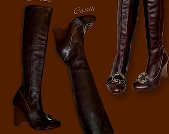 May include: Three pairs of brown leather knee-high boots with gold buckles. The boots have a wedge heel and a pointed toe. The text "Just Cavalli" is visible on the image.