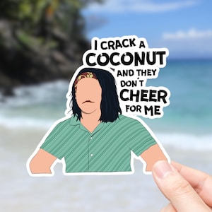 May include: A sticker featuring a cartoon illustration of a person with long black hair wearing a green striped shirt and a red bandana. The text on the sticker reads "I crack a coconut and they don't cheer for me."