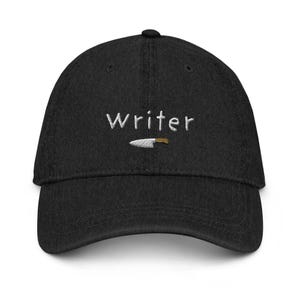 May include: A black denim baseball cap with white embroidery that reads "Writer" and a small knife graphic.