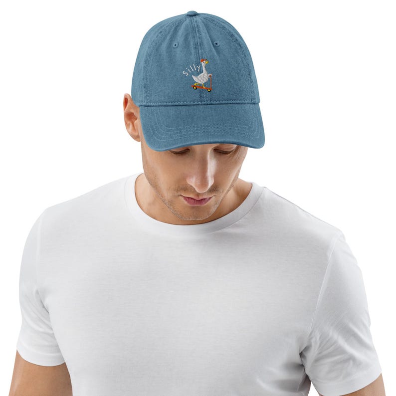 Puede incluir: Una gorra de b&eacute;isbol de mezclilla azul con un ganso bordado en blanco montando un scooter y la palabra "silly" arriba.