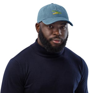 Pu&ograve; includere: Una persona indossa un cappello da baseball in denim blu con un alligatore verde ricamato e il testo "Oh Snap!" in bianco. La persona indossa un maglione a collo alto blu scuro.