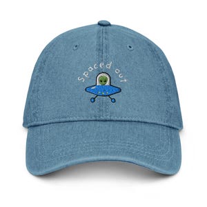 May include: A blue denim baseball cap with white embroidery that says "Spaced out" and a cartoon alien in a flying saucer.
