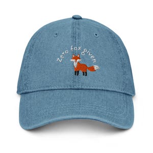 May include: A blue denim baseball cap with white embroidery that reads "Zero fox given" and features a small embroidered orange fox.