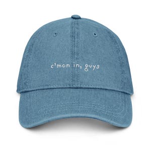 May include: A blue denim baseball cap with white embroidered text that reads "c'mon in, guys".