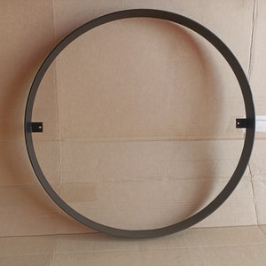 Könnte beinhalten: Ein dunkelgrauer Metallring mit zwei kleinen rechteckigen Montagehalterungen. Der kreisförmige Rahmen besteht aus einem dicken, robusten Material. Das Objekt ist für Wanddekorationen oder ähnliche Zwecke bestimmt.