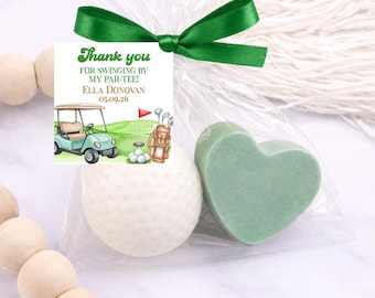 May include: A clear plastic favor bag tied with a green ribbon containing a white golf ball and a light green heart-shaped soap. A square tag attached reads: Thank you FOR SWINGING BY MY PAR-TEE! ELLA DONOVAN 05.09.26, featuring a golf cart illustration.